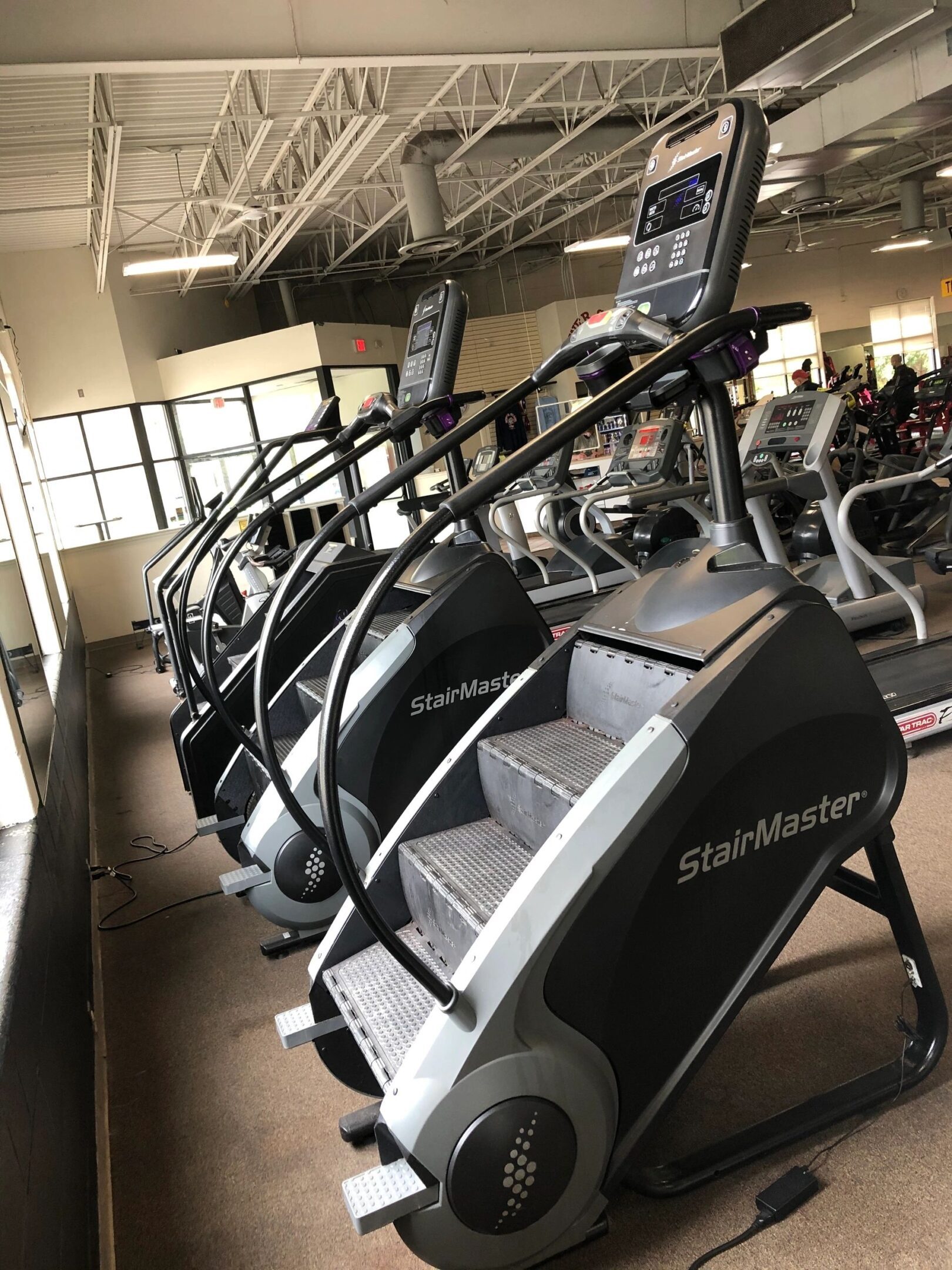 Three StairMaster machines lined up in a gym, facing a window.