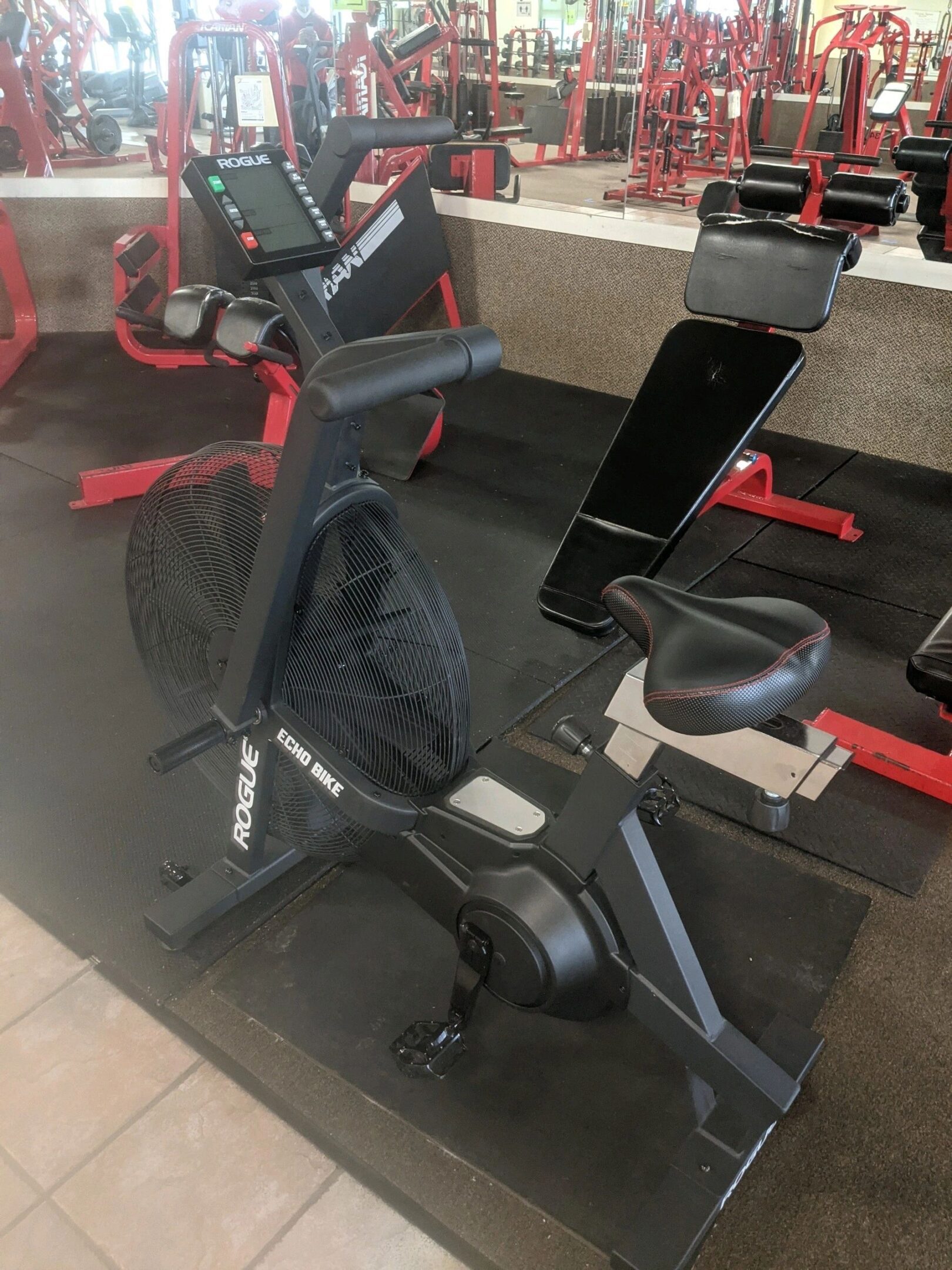 Exercise bike in a gym setting with red and black equipment in the background.
