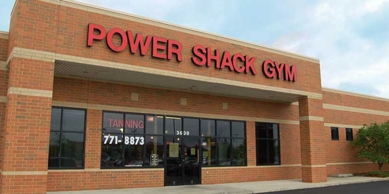 Exterior of Power Shack Gym, a brick building with large windows. The words "Tanning" and a phone number are displayed on the window.