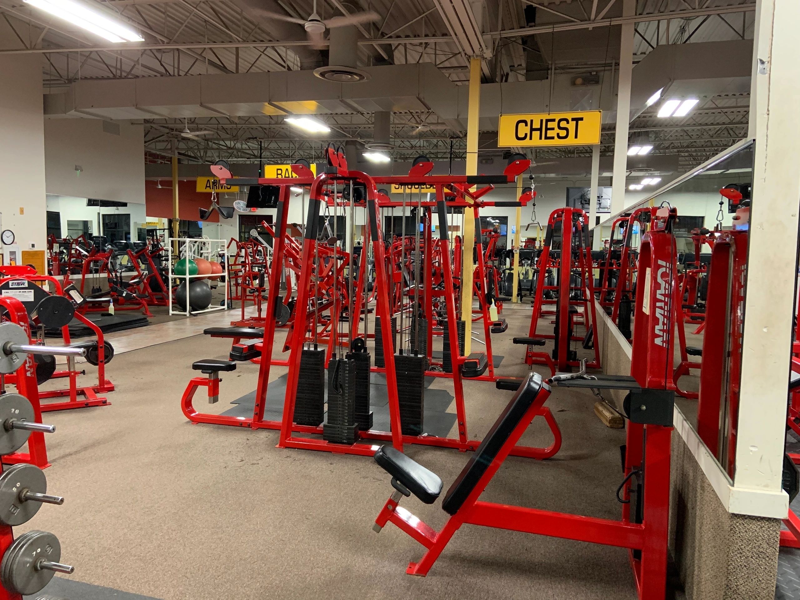 A gym with various red exercise machines, including weight lifting equipment, under a sign labeled "Chest.