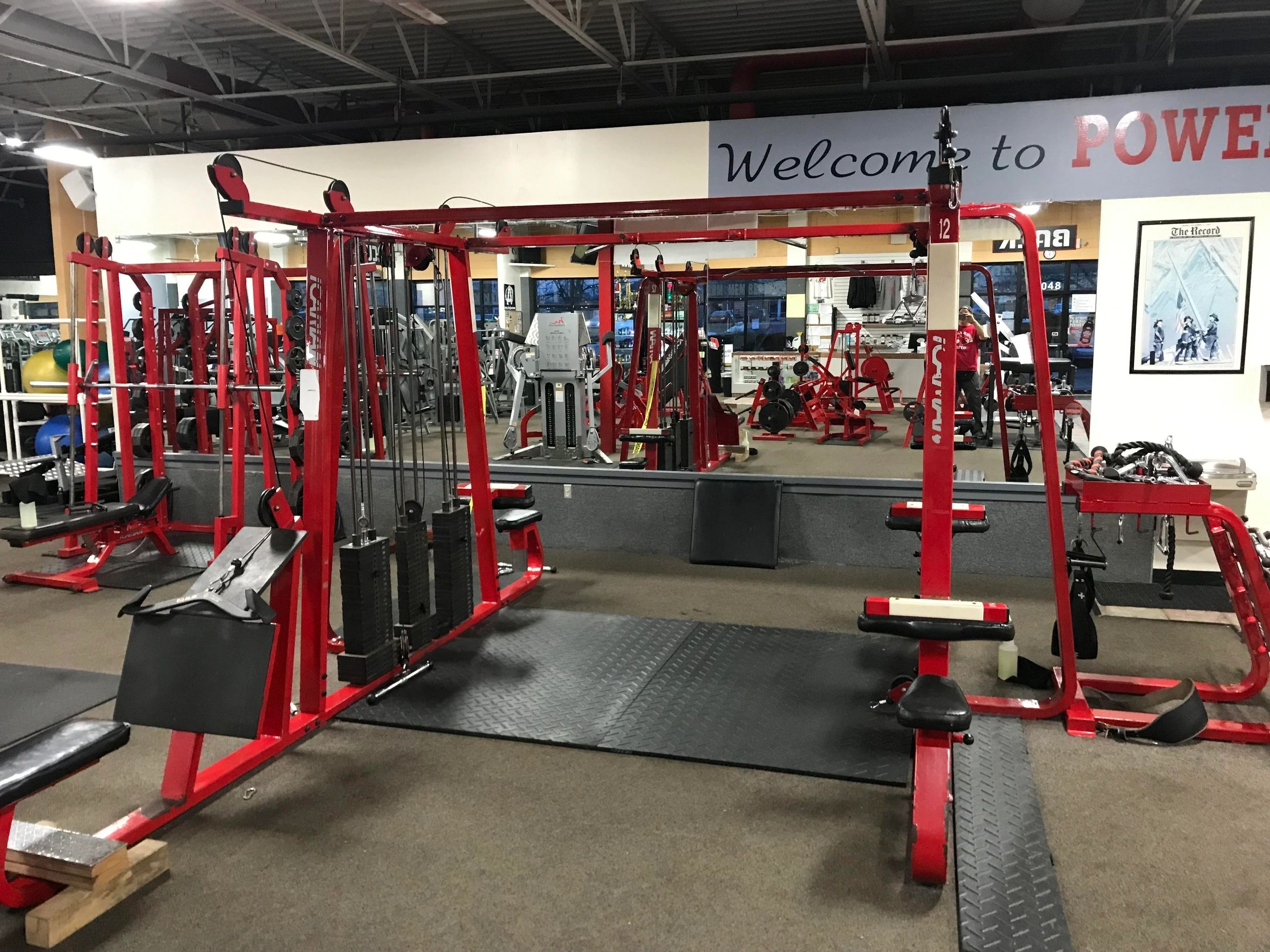 A gym with red exercise equipment, mirrors on the walls, and a sign that reads "Welcome to Power.