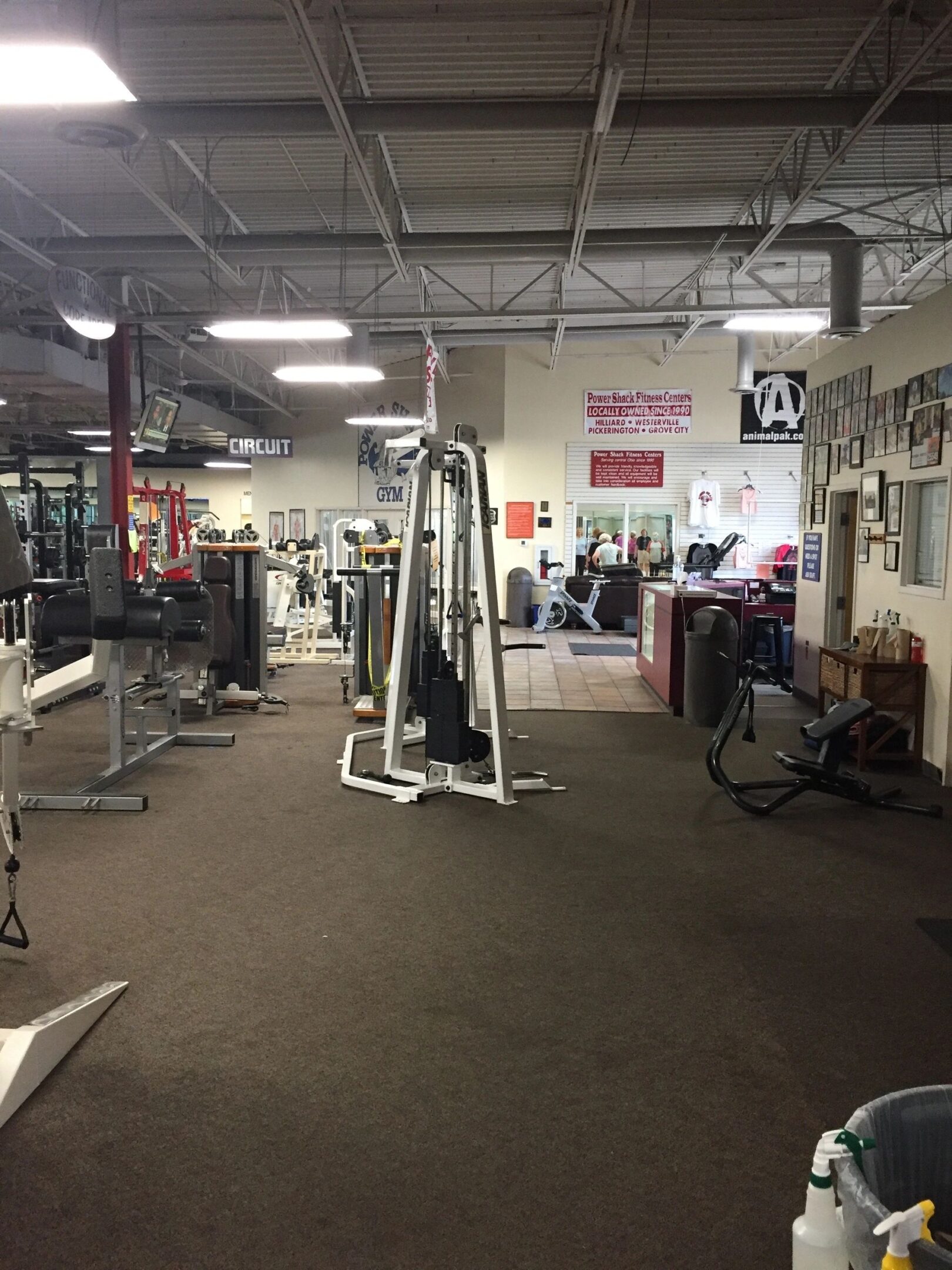 A gym with various exercise machines, including a cable machine, weight benches, and treadmills. The room has high ceilings and wall mirrors.
