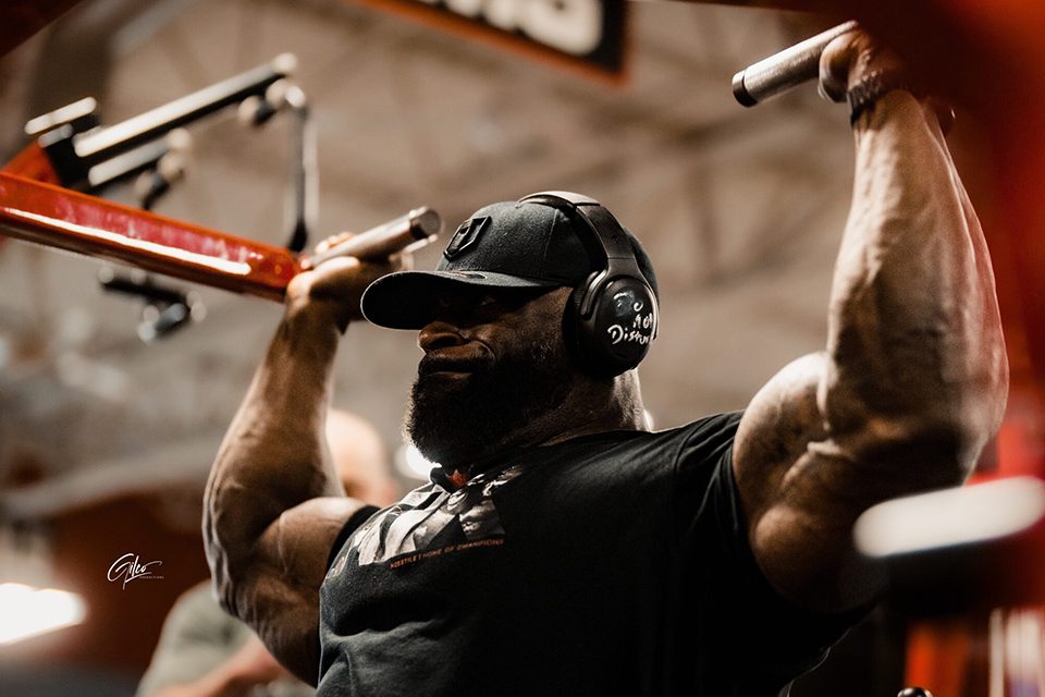 _0000_Samson-Dauda-2048x1638 A man with headphones on is doing shoulder press.